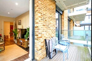 Ein Zimmer mit Backsteinwand, einem Balkon mit Sitzgelegenheiten, Holzboden und einem großen Fenster.