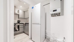 Eine moderne Küche mit einem weißen Kühlschrank, einem eingebauten Ofen und einem wandmontierten digitalen Thermostat.