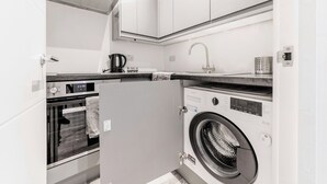 Eine kompakte Küche mit eingebautem Ofen, Waschmaschine und Kaffeemaschine.