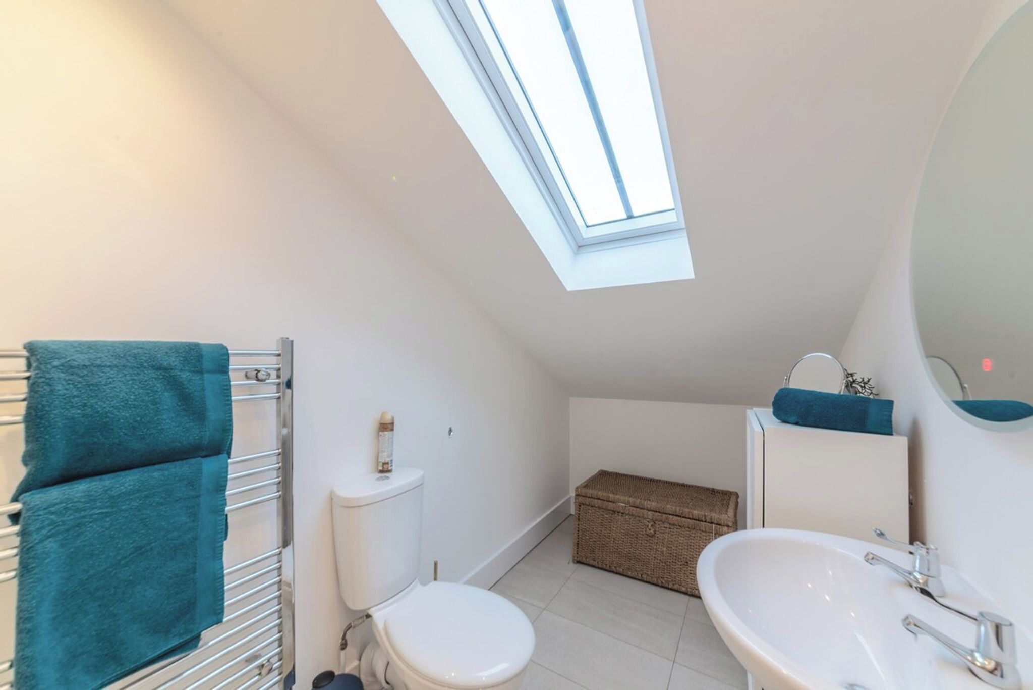 A small, modern bathroom with a skylight, a toilet, a sink, and a wicker basket.