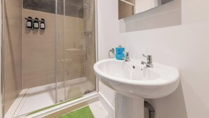 A bathroom with a glass shower enclosure, a white sink, and a mirror above it. - Cosy Serene Flat near the City Centre (Kent)