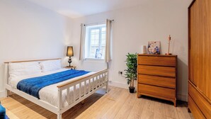 A bedroom with a bed, a dresser, a window with curtains, a lamp, and a potted plant. - Cosy Serene Flat near the City Centre (Kent)