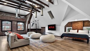 Una camera da letto in stile loft con travi a vista, un'ampia finestra, un letto, un divano e una televisione.