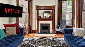 Un soggiorno con camino, due divani blu, un tavolino da caffè e una televisione che mostra 'NETFLIX'.