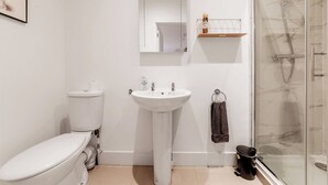 Un baño con inodoro, lavabo, espejo, ducha y toallero.