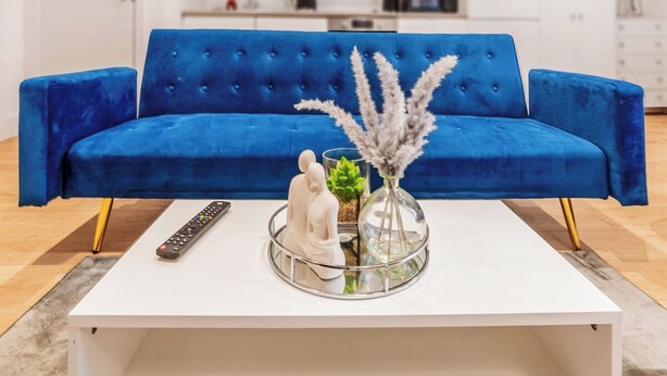 Un sofá azul, una mesa de centro blanca, un control remoto y objetos decorativos.