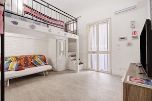Ein Zimmer mit Etagenbett, einer Schlafcouch, einem Fernseher und einer Treppe.