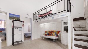 A loft-style room with a white brick wall, a white sofa with colorful cushions, a metal shelf unit, and a staircase with a black railing. - Holiday Home 'Ciccina' with Wi-Fi and Air Conditioning (Palermo)
