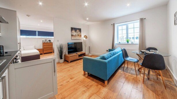 Una sala de estar moderna con sofá, televisor, mesa de comedor y ventana con cortinas.