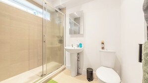 Un baño con cabina de ducha de vidrio, lavamanos, inodoro y espejo.