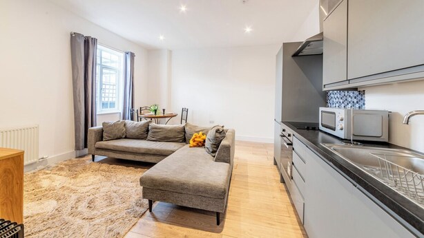 Een modern appartement met een bank, voetenbankje, keuken en eethoek.