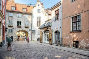 Eine Kopfsteinpflasterstraße mit historischen Gebäuden, darunter ein Gebäude mit einem großen Rundbogenportal und ein weiteres mit einer Holztür.