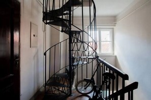 Eine Wendeltreppe mit einem Fahrrad, das dagegen gelehnt ist, einer Tür links und einem Fenster rechts.