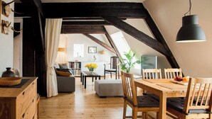 Un espace de vie de style « loft », avec des poutres apparentes, un coin repas doté de meubles en bois, et une vue sur la cuisine et l’espace de vie.