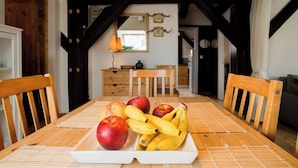 Une table à manger en bois, sur laquelle se trouve un plateau de fruits, des chaises en bois, un buffet en bois et un miroir accroché au mur.