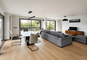 En moderne stue med en stor grå sofa, et spisebord med stole, et fjernsyn og et træskab.