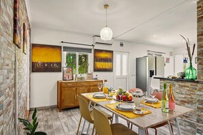 A modern kitchen with a dining table set for four, a hanging light fixture, and a brick wall. - Villa 'Casa Do Sol' in Tavira (Luz)