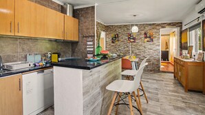 A modern kitchen with wooden cabinets, a dishwasher, a black countertop, and a dining area with chairs. - Villa 'Casa Do Sol' in Tavira (Luz)