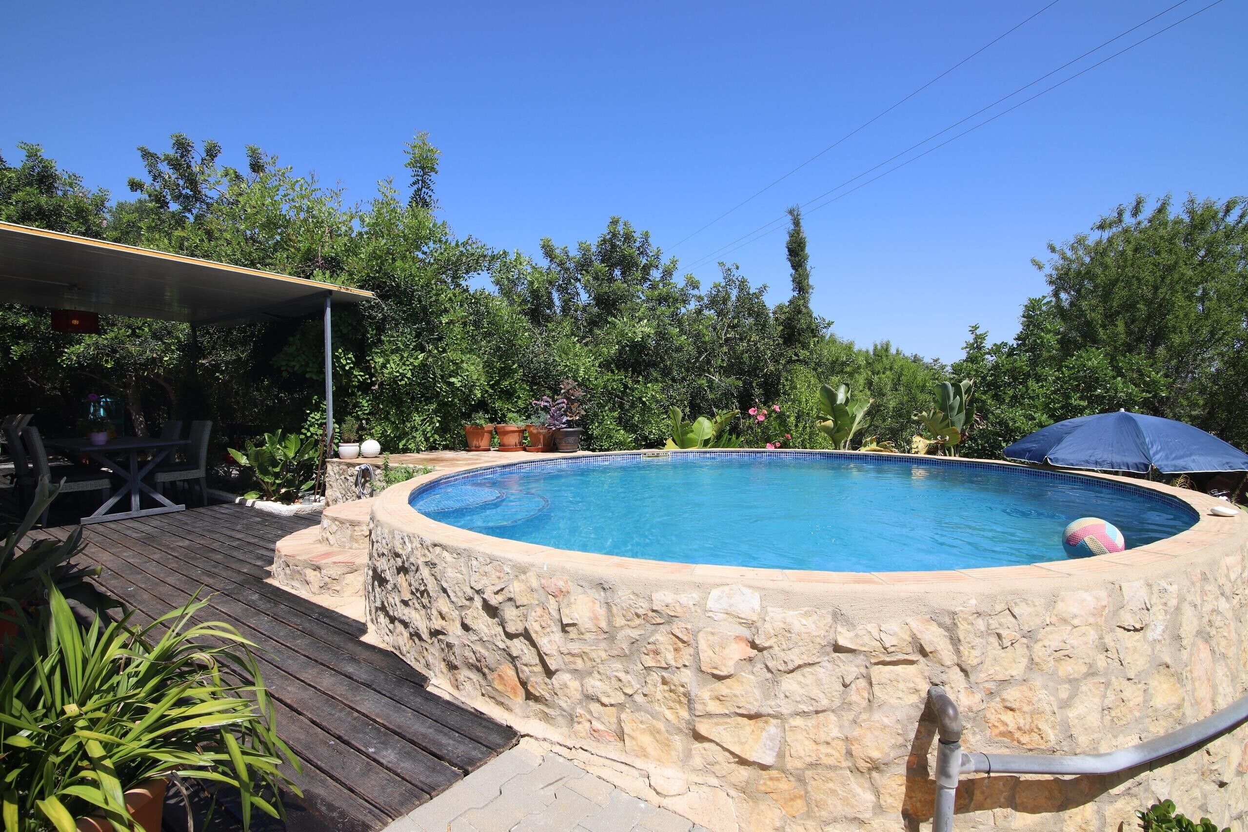 A swimming pool with a stone wall, surrounded by a wooden deck and potted plants.