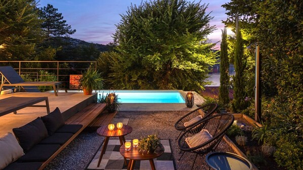 Un espace aménagé au bord de la piscine, avec des chaises longues, une table décorée de bougies et une vue sur une étendue d’eau.