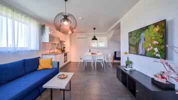 Un appartement moderne avec un canapé bleu, une table à manger dressée pour quatre personnes, une cuisine en arrière-plan et un grand tableau représentant un paysage naturel accroché au mur.
