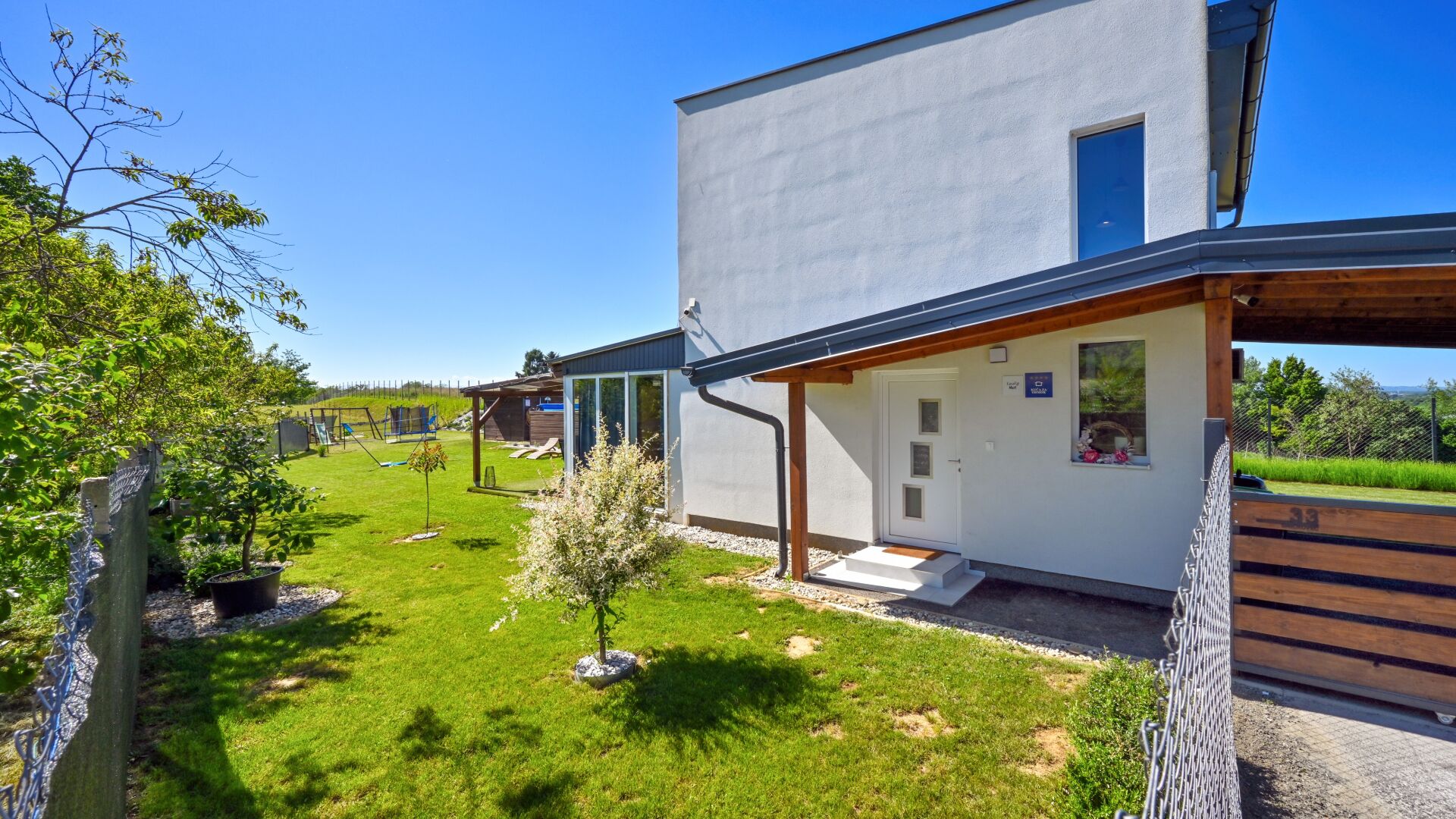 Une maison moderne à deux étages, dotée d’un porche abrité, d’un petit jardin et surplombant un ciel d’un bleu éclatant.