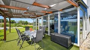 A covered patio with a table and chairs, a grill, and a view through glass walls. - Villa Una by Villas Guide (Gornji Kneginec)