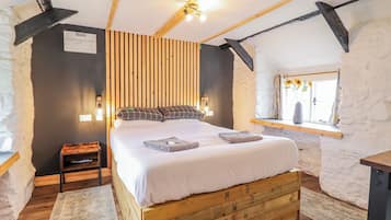 A bedroom with a wooden bed, a nightstand, a window with a view, and a sloped ceiling.