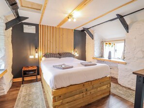 A bedroom with a wooden bed, a nightstand, a window with a view, and a sloped ceiling.