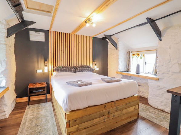 A bedroom with a wooden bed, a nightstand, a window with a view, and a sloped ceiling.