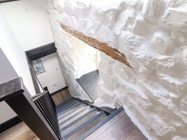 Una escalera con pared blanca con textura, suelo de madera y barandilla de metal.