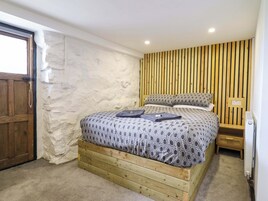 Un dormitorio con una cama de madera, una pared blanca con textura y un cabecero de madera con listones.