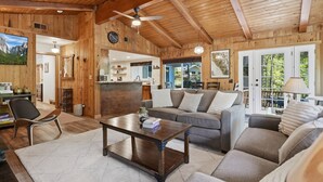 Indretning i en hyggelig hytte med træloft, sofa, sofabord og spiseplads.