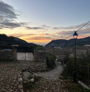 A stone pathway leading to a gated entrance, a lamp post, and a view of a village with buildings and hills in the background. - Typical village house in Valldemossa (Valldemossa)