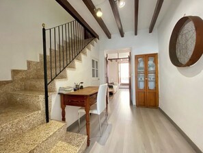 A staircase with a black railing, a wooden dining table with chairs, and a wooden door with glass panels. - Typical village house in Valldemossa (Valldemossa)