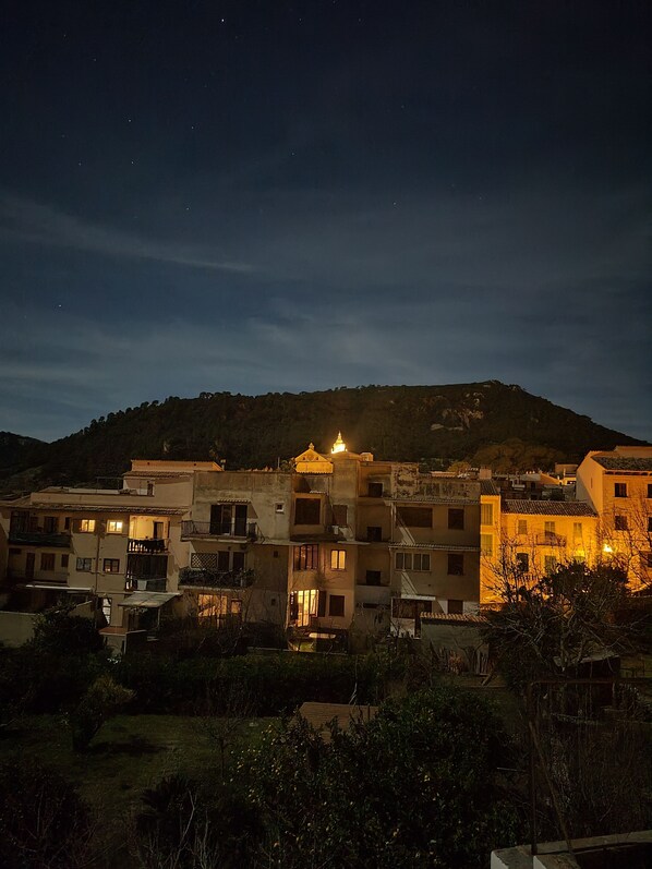 A nighttime view of a residential area with buildings, a hill in the background, and a lit building in the foreground. - Typical village house in Valldemossa (Valldemossa)
