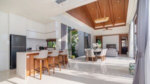 A modern kitchen with a central island, bar stools, and a dining area with a table and chairs. - Ozone Sanctuary 3BR Private Pool Villa (Choeng Thale)