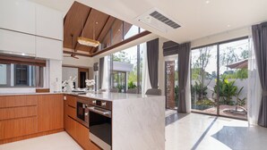 A modern kitchen with wooden cabinets, a marble countertop, and a built-in oven. - Ozone Sanctuary 3BR Private Pool Villa (Choeng Thale)