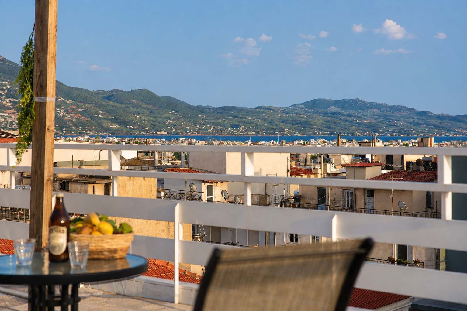 A terrace with a table, chairs, and a view of a coastal town and mountains.