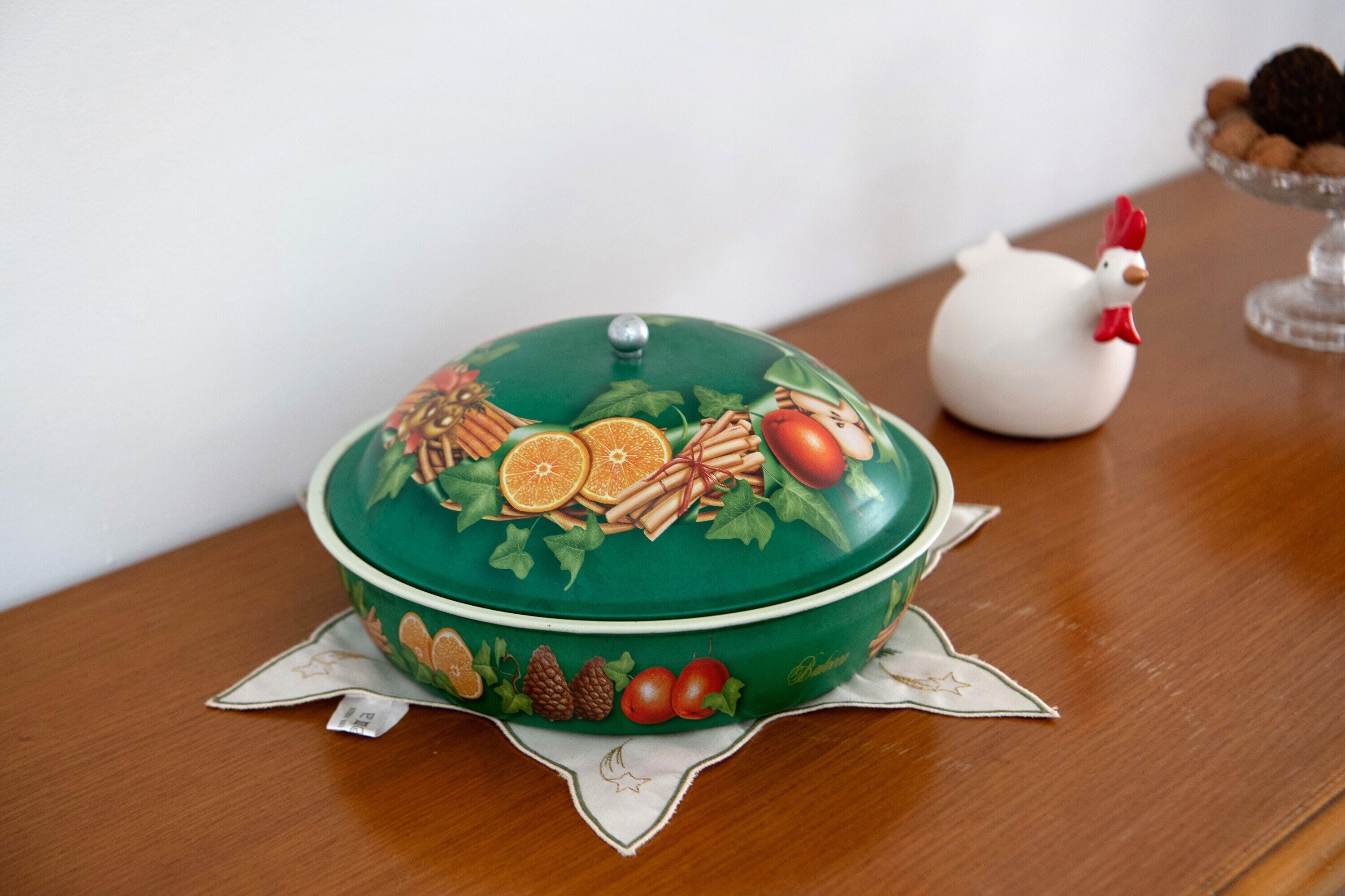 A green covered container with fruit designs on a wooden table.