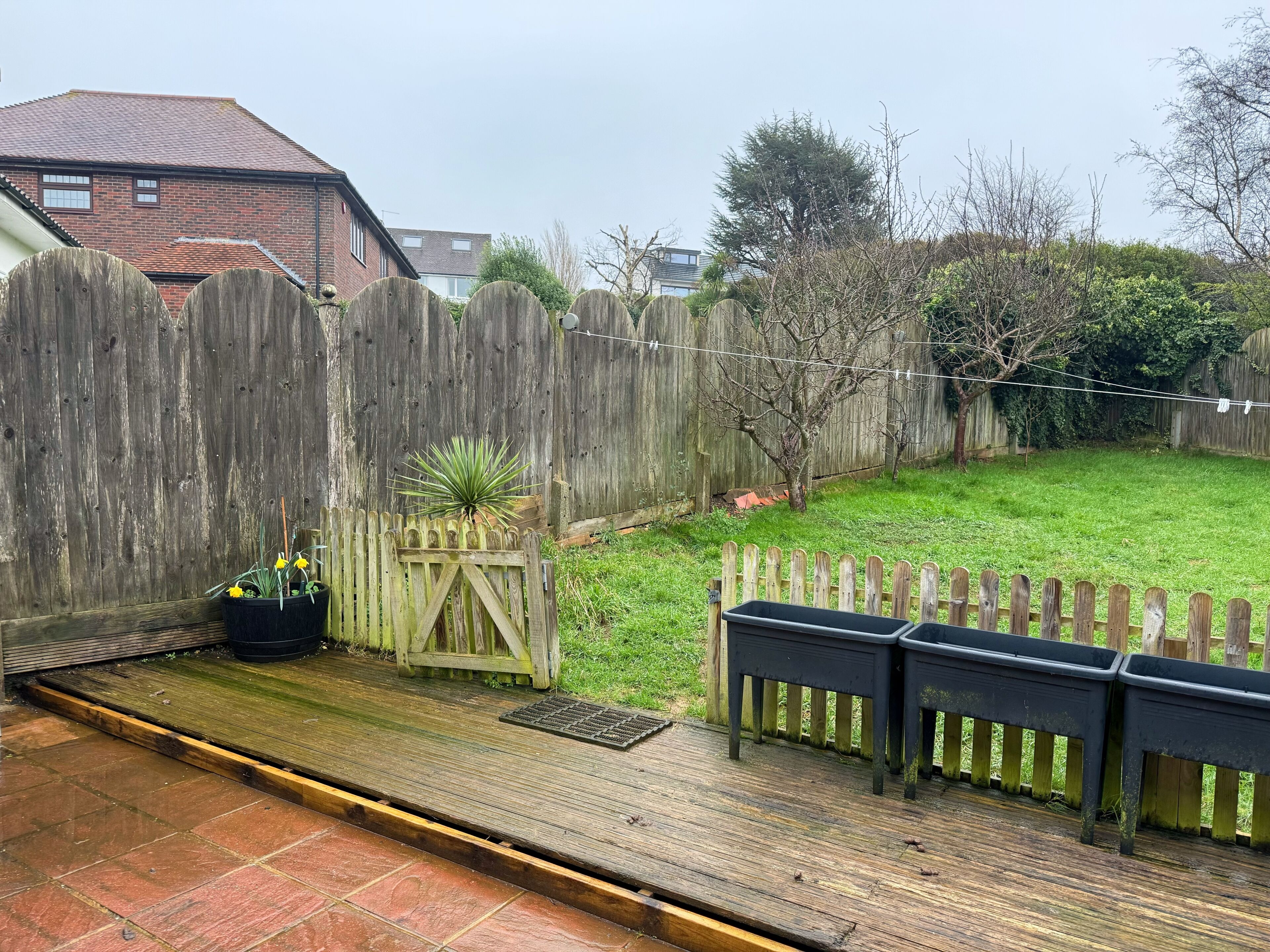 A wooden deck with a metal grate, a small garden with a plant, and a wooden fence.