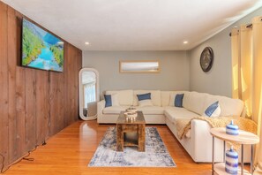 Un salon avec un canapé blanc, une table basse en bois, un tapis et un tableau accroché au mur.