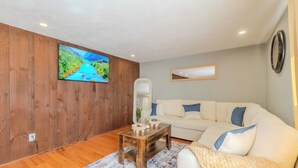 Ein Wohnzimmer mit Holzwand, einem weißen Sofa, einem Couchtisch, einem Fernseher und einem Spiegel.
