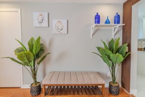 Une pièce comprenant un banc, deux plantes en pot et deux œuvres d’art accrochées au mur.