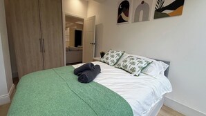 A bedroom with a bed, green blanket, pillows, and artwork on the wall. - 2 Bed - Sleeps 5 - Garden - Hot-tub (London)