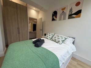 Een slaapkamer met een bed, een groene deken, kussens en kunst aan de muur.