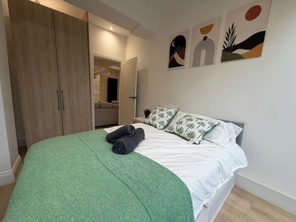 Un dormitorio con cama, manta verde, almohadas y una obra de arte en la pared.