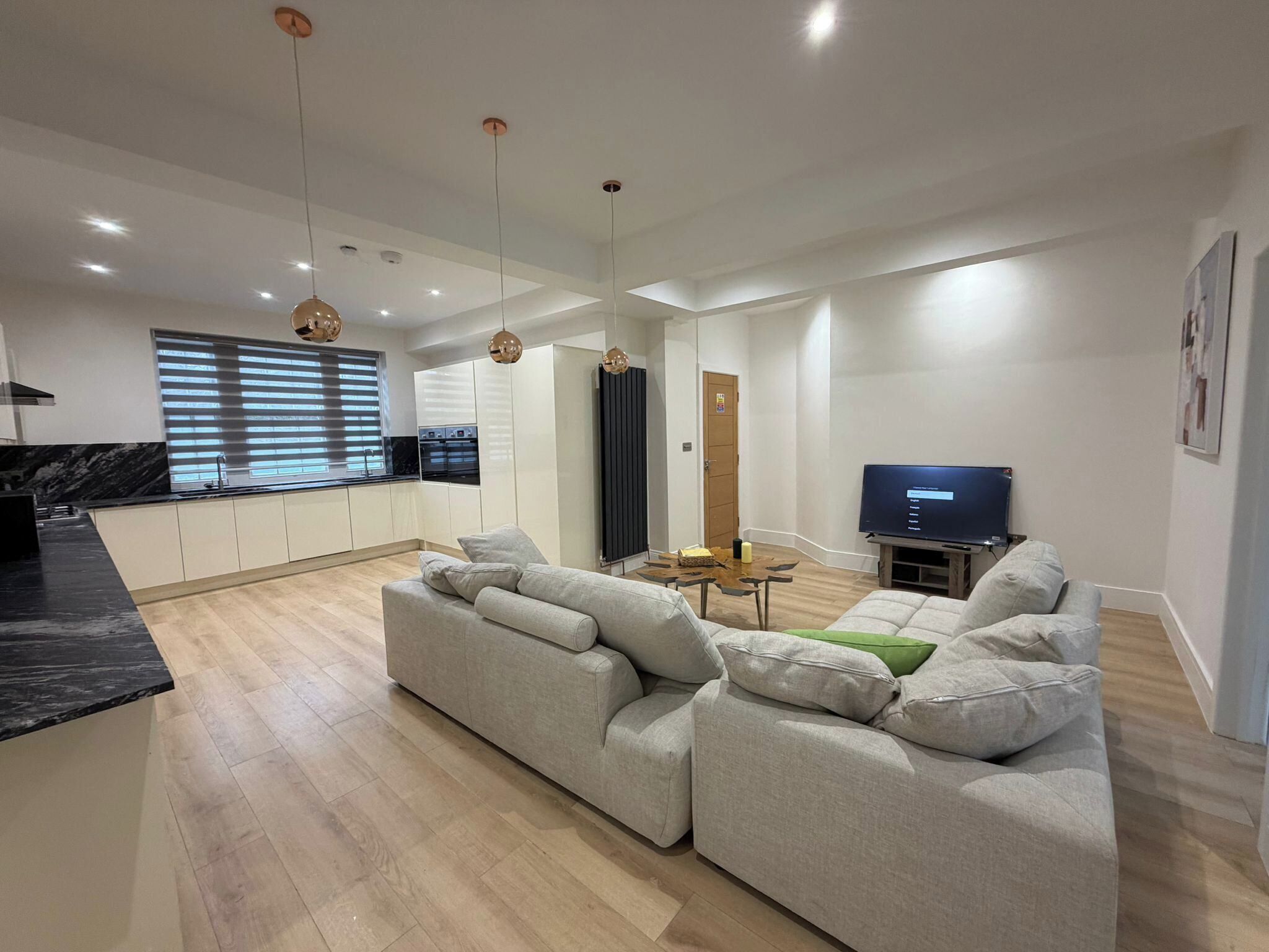Een moderne woonkamer met een bank, een televisie en een keukenhoek met kasten en een raam.