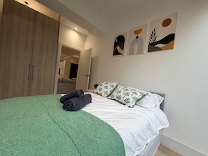 A bedroom with a bed, green blanket, pillows, and artwork on the wall. - 2 Bed - Sleeps 5 - Garden - Hot-tub (London)