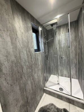 A modern shower enclosure with a glass door and a small window, set against a textured wall. - 2 Bed - Sleeps 5 - Garden - Hot-tub (London)